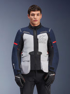 Alpinestars ST-7 2L GORE-TEX-jacka, motorcykeljacka för äventyrstouring, isgrå och mörkblå med röda detaljer, vattentät och andningsbar, bärs av en modell med svarta handskar, med Alpinestars Exploration Equipment-logotyp på bröstet