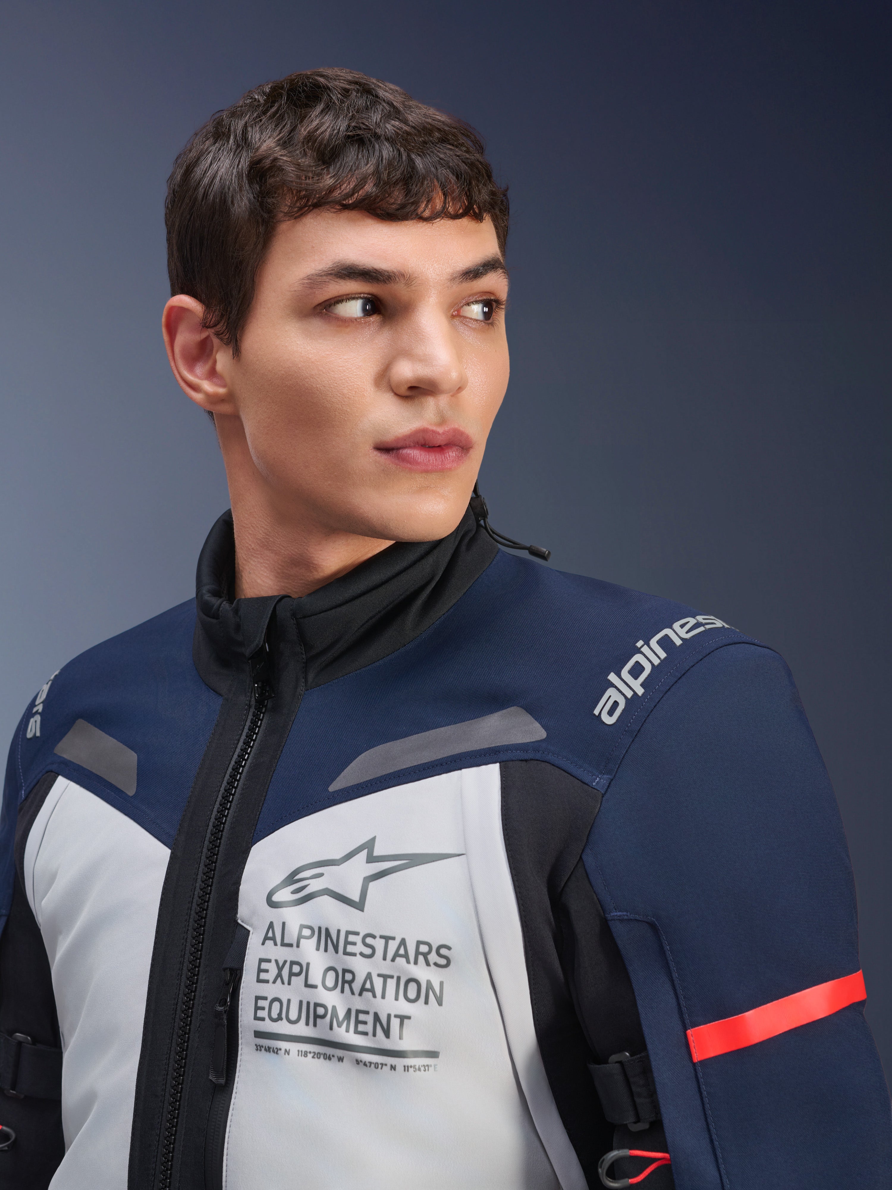 Alpinestars ST-7 2L GORE-TEX-jacka, Ice Gray, mörkblå och svart, bärs av manlig modell, med Alpinestars Exploration Equipment-märkning på bröstet, hög krage och röd accent på ärmen, hållbar textildesign för adventure touring