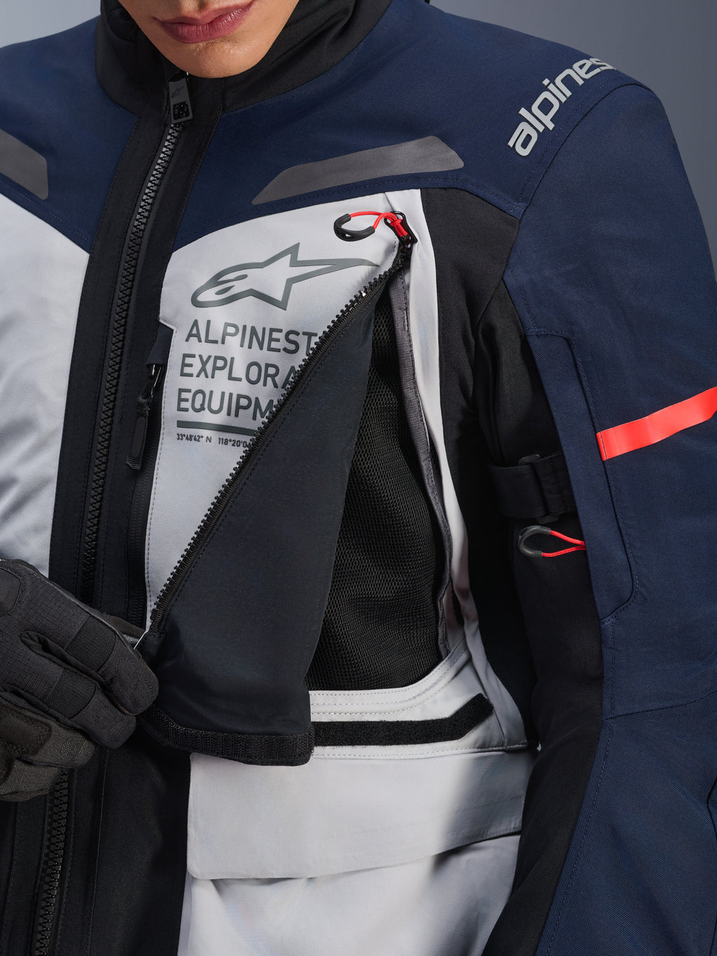 Alpinestars ST-7 2L GORE-TEX-jacka, Adventure Touring-jacka, Ice Gray, Dark Blue och svart, detaljvy av den öppnade ventilationspanelen på bröstet som visar svart mesh, med Alpinestars Exploration Equipment-logotyp och röda dragtappar