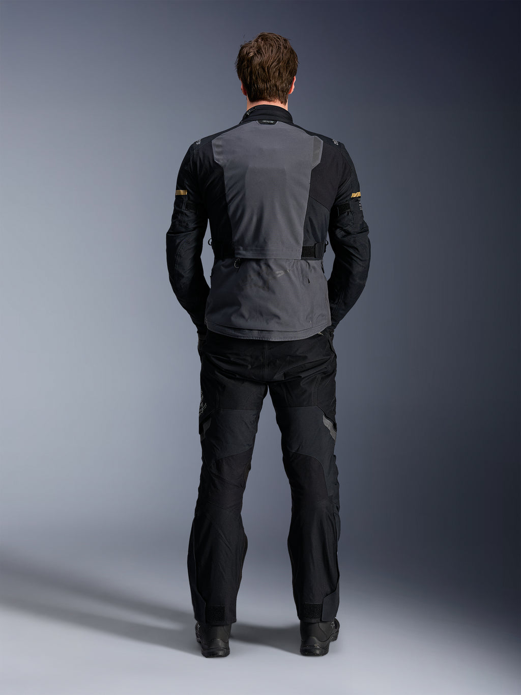 Alpinestars ST-7 2L GORE-TEX-jacka, Deep Gray Black och Dark Khaki, baksida på en modell, adventure-motorcykeljacka för touring med grå ryggpanel och svarta förböjda ärmar, bärs med matchande svarta byxor.