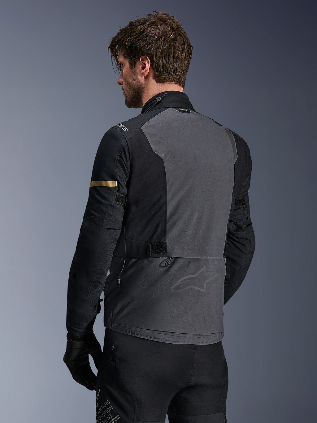 Alpinestars ST-7 2L GORE-TEX-jacka, motorcykeljacka, Deep Gray Black och Dark Khaki, vy bakifrån som visar stor grå ryggpanel med subtilt varumärke, svarta ärmar med guldfärgade khaki-detaljer, äventyrsklar vattentät textildesign