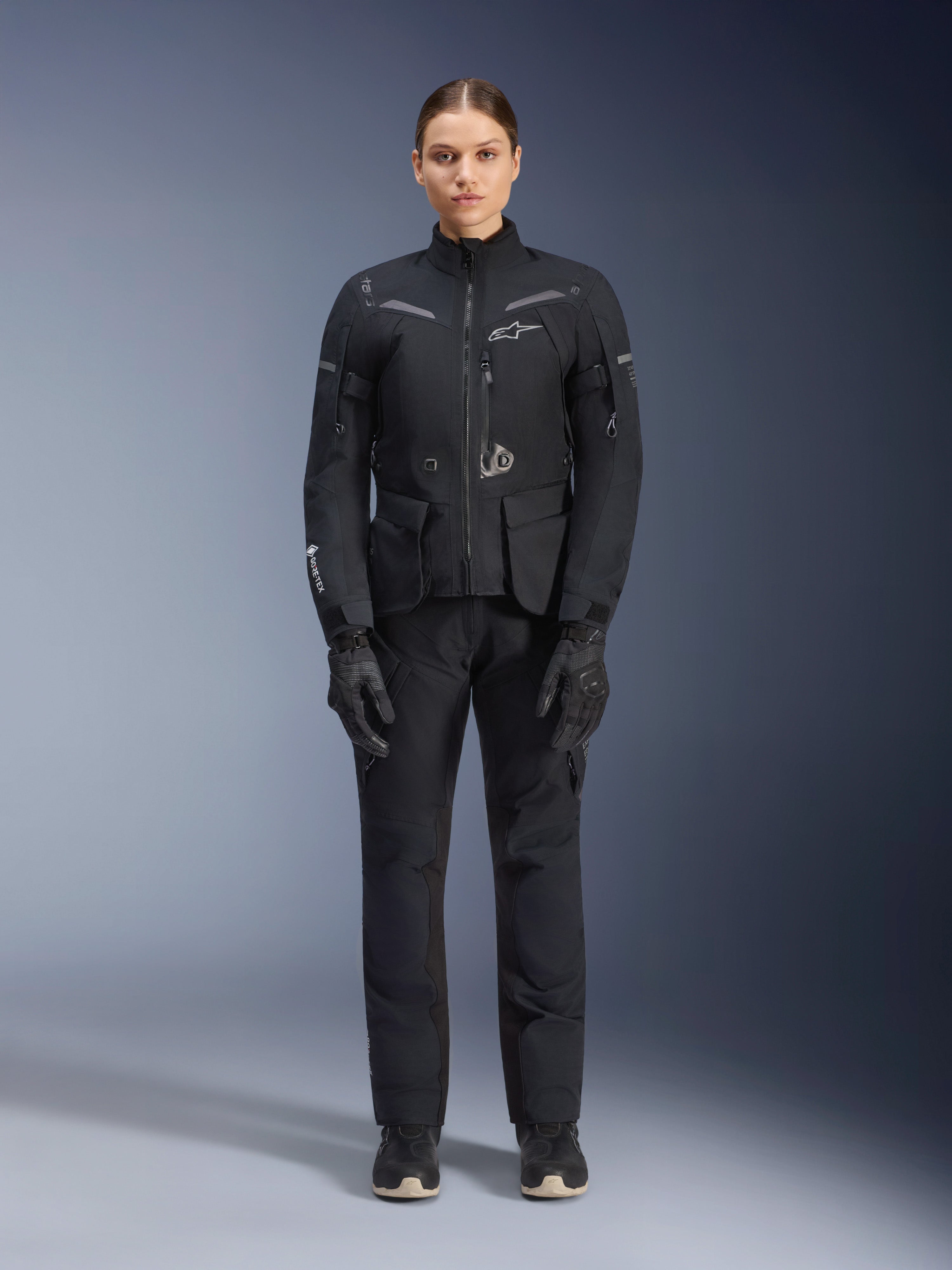 Kvinnlig förare som bär Alpinestars Stella ST-7 2L GORE-TEX jacka och byxor, svart touring-outfit för motorcykel, vattentät och andningsbar teknisk utrustning, matchande svarta handskar och stövlar, heltäckande skyddsutrustning med reflekterande detaljer, modern teknisk design för äventyrskörning