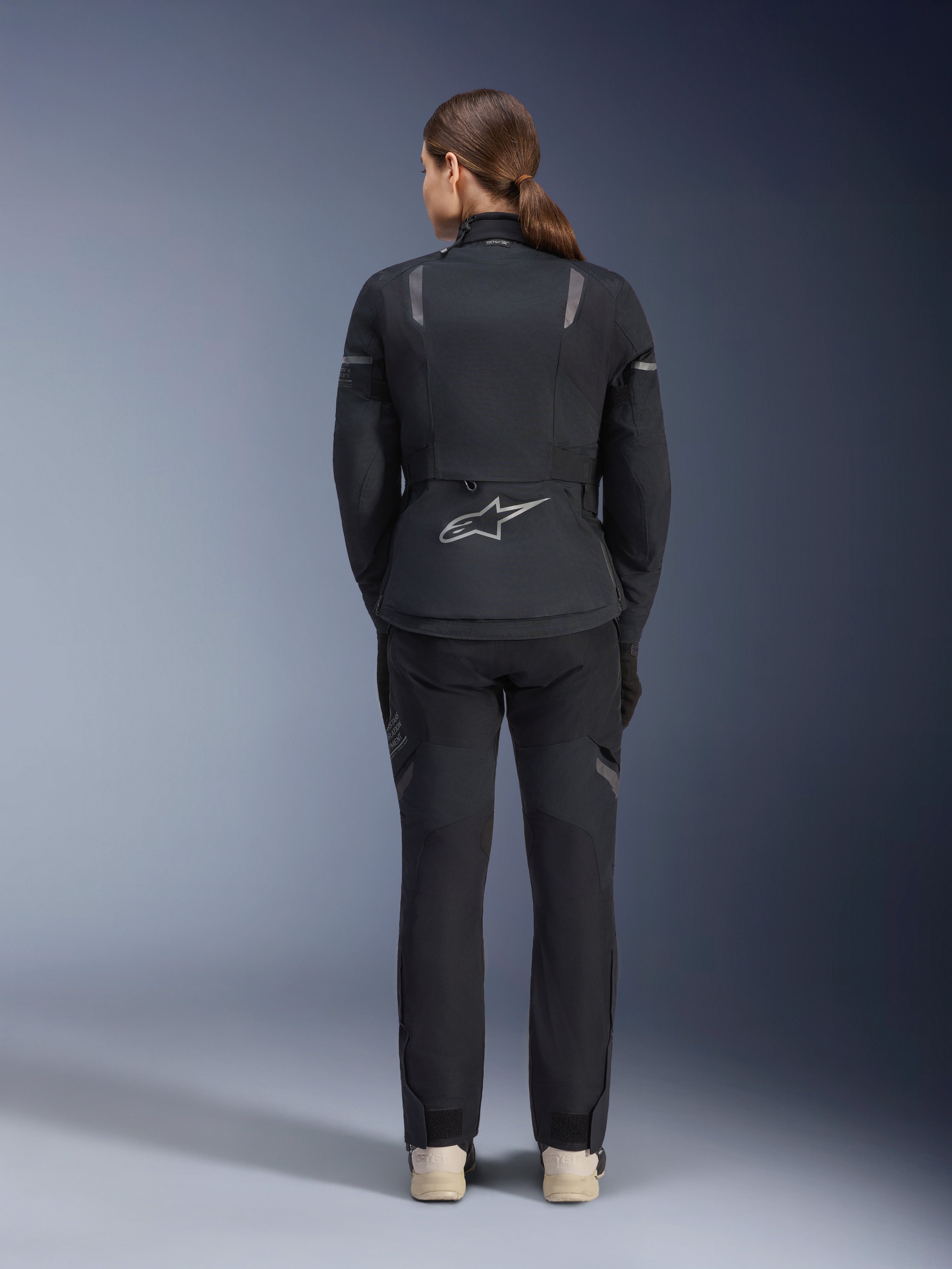 Alpinestars Stella ST-7 2L GORE-TEX-jacka för damer, svart och mörkgrå, ryggvy med den silvriga Alpinestars-logotypen på nedre ryggen, matchad med svarta textilbyxor, adventure touring-motorcykelutrustning