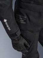 Alpinestars Stella ST-7 2L GORE-TEX-jacka för dam, svart äventyrs- och touringjacka, närbild av ärm med vit GORE-TEX-logotyp, Alpinestars Exploration Equipment-text på höften, svart motorcykelhandske, vattentätt textilmaterial med funktionella cargofickor