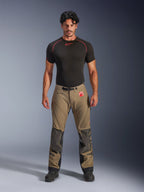 Manlig modell bär Alpinestars Nazca 3L GORE-TEX PRO-byxor i valnötsbrunt och svart, teknisk äventyrsutrustning med Superfabric-knäförstärkningar och ett magnetiskt midjespänne, kombinerat med en svart Alpinestars-undertröja, studiovy framifrån.