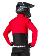 Alpinestars Lite-Dura Softshell Jacket, Black Bright Red White, back view on a motocross rider, red upper body and sleeves with black lower back panel, zippered rear storage pocket, white Alpinestars logo on the bottom hem, worn with a black helmet and pants