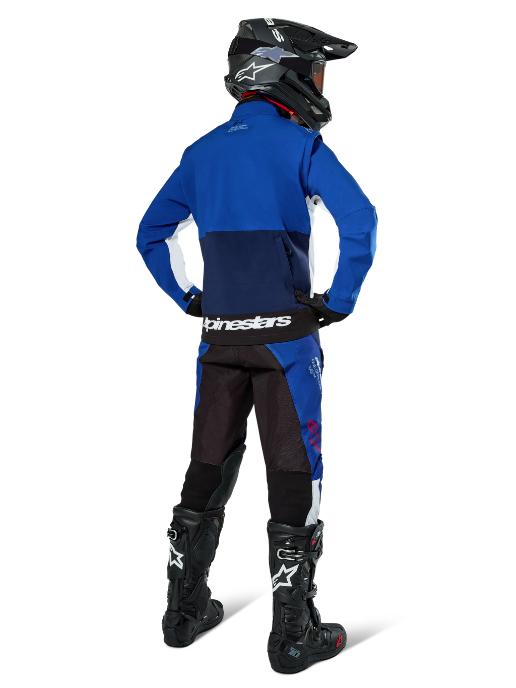 Motocross rider from behind wearing Alpinestars Lite-Dura Softshell Jacket in Navy Bright Blue and White, paired with matching enduro pants, black helmet, and black boots, complete off-road racing gear