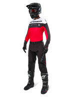 Alpinestars Pro-Dura-byxor i Black Magnet White, bärs av en förare med matchande röd, svart och vit tröja, svart hjälm och svarta offroad-stövlar, komplett professionell enduro-racingutrustning för terrängprestanda.