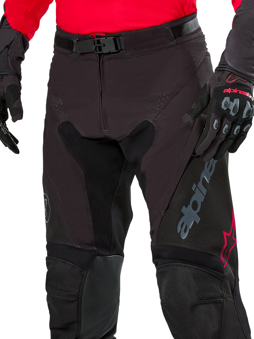 Närbild på Alpinestars Pro-Dura-byxor, endurobyxor, Black Magnet White med röda detaljer, med ett säkert magnetspänne och gylf med dragkedja, bärs med matchande röd tröja och svarta handskar, slitstark ripstop-konstruktion för terrängkörning