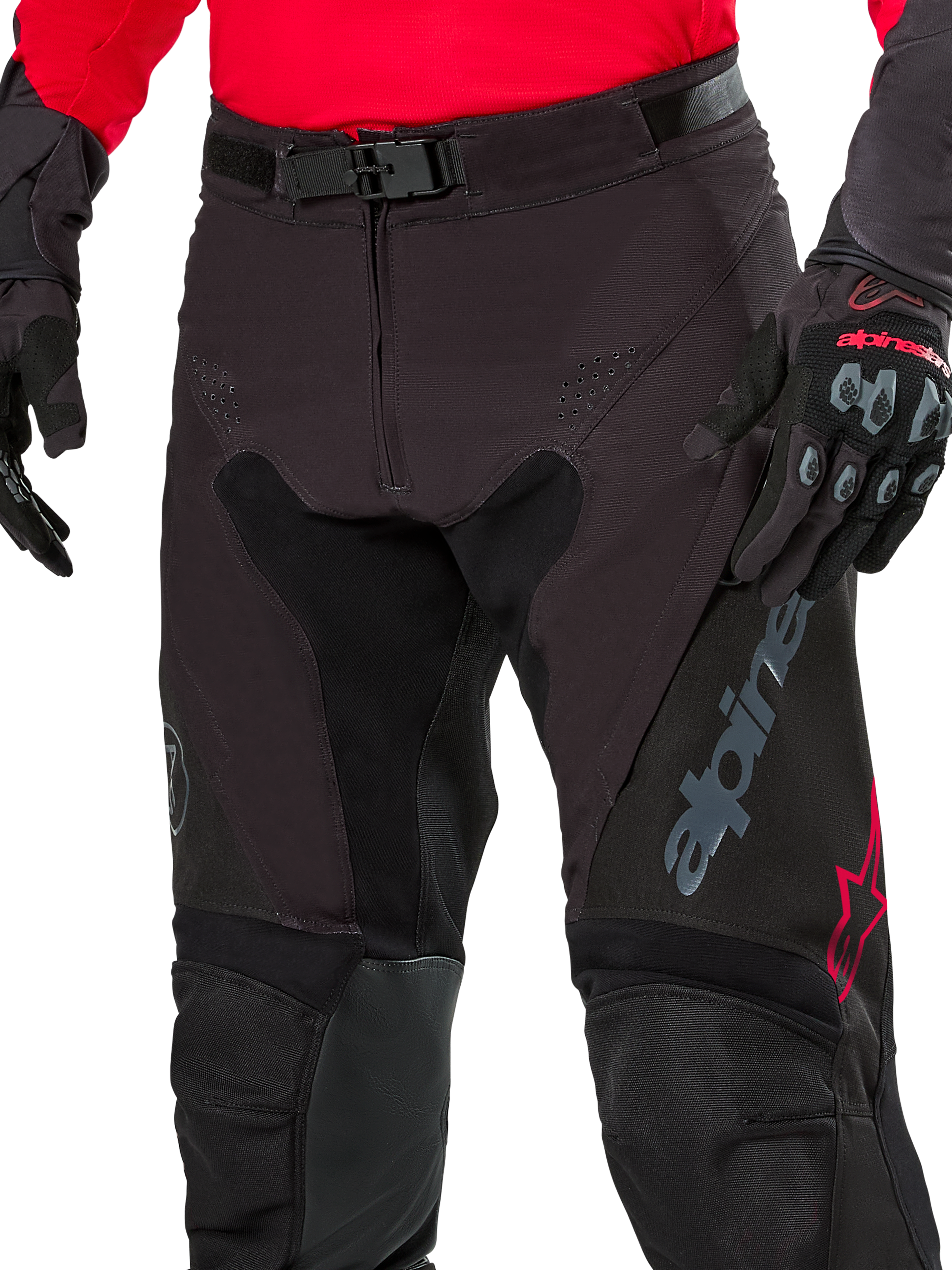Närbild på Alpinestars Pro-Dura-byxor, endurobyxor, Black Magnet White med röda detaljer, med ett säkert magnetspänne och gylf med dragkedja, bärs med matchande röd tröja och svarta handskar, slitstark ripstop-konstruktion för terrängkörning