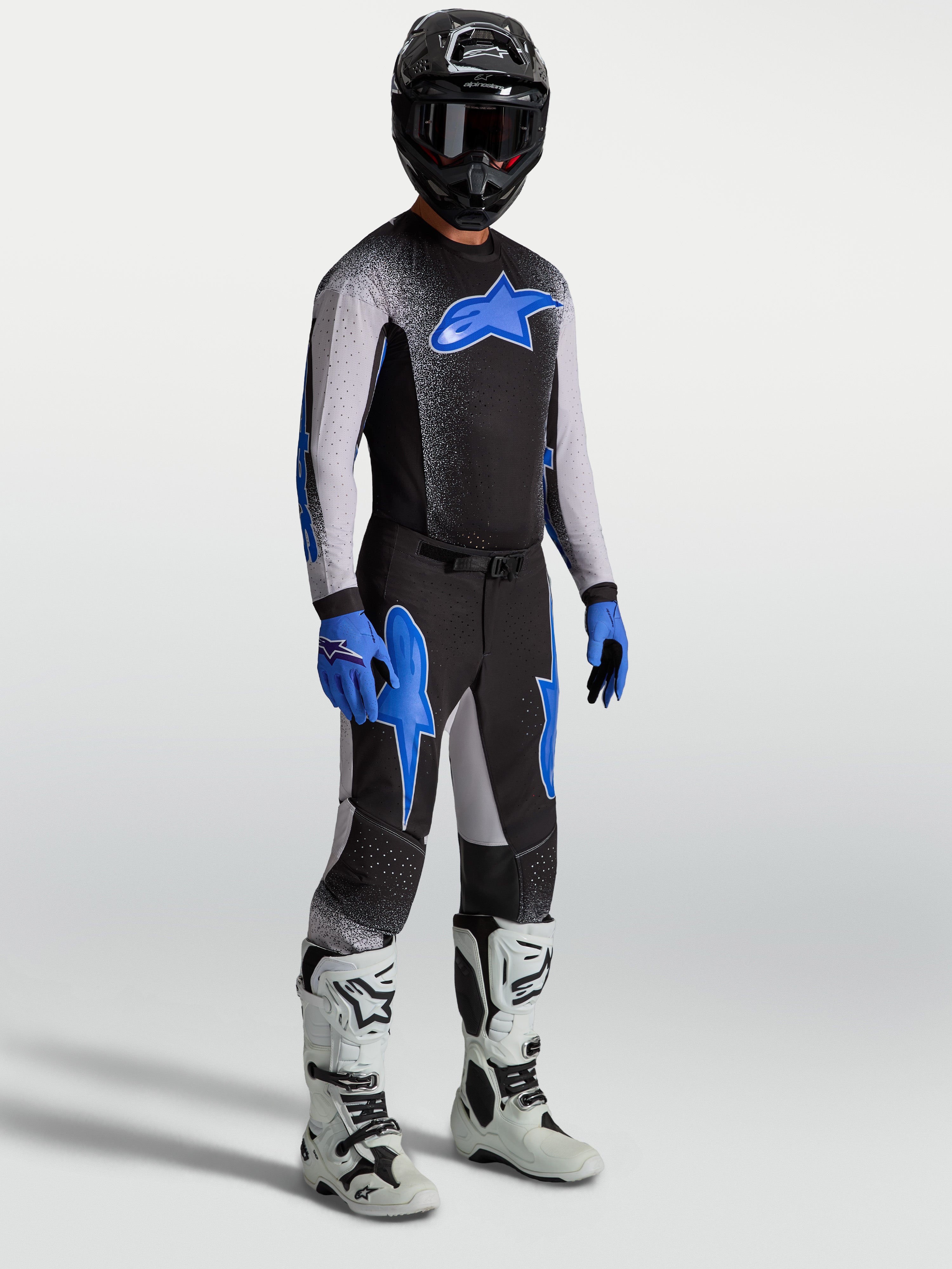 Alpinestars Supertech Hiten AFD byxor, motocrossbyxor på modell med matchande tröja och vita stövlar, svarta och blå.