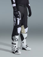Alpinestars 2026 Racer Air Riway byxor, motocrossbyxor, svarta och vita, bärs med vita och svarta Tech Series-stövlar och svart långärmad tröja, med vita Alpinestars-logotyper, laserskurna perforeringar och beige innerpaneler i getskinn på knäna för terrängprestanda.
