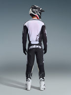 Motocrossförare sedd bakifrån bär Alpinestars 2026 Racer Air Riway-byxor i svart och vitt, matchande svartvit långärmad tröja, vita och svarta racingstövlar och en svart hjälm med Alpinestars-märkning.