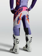 Alpinestars Supertech Dyna byxor, lila motocrossbyxor för herrar med orange grafik, sedda bakifrån med vita stövlar