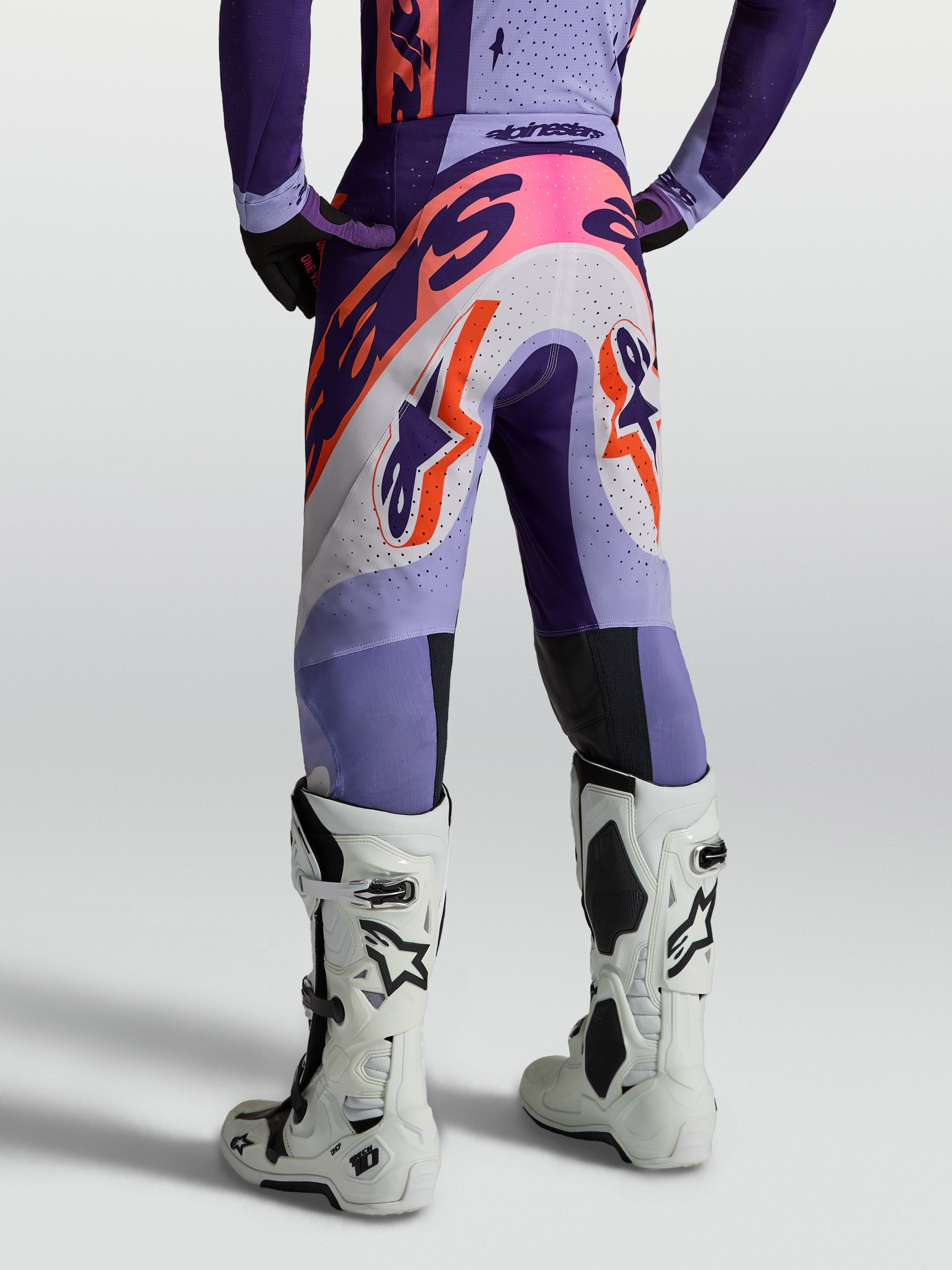 Alpinestars Supertech Dyna byxor, lila motocrossbyxor för herrar med orange grafik, sedda bakifrån med vita stövlar