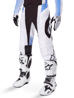 Alpinestars 2025 Techstar Melt Pants, Motocross Pants, White and Black with Blue accents, featuring laser-cut perforations for airflow and Babel knee construction, worn with matching white motocross boots and gloves, athletic off-road racing design