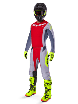Motocrossförare iklädd Alpinestars 2025 Techstar Melt-utrustningsset, röd och grå tröja och byxor, vibrerande neongula handskar och stövlar, svart hjälm, komplett racingutrustning för terrängkörning