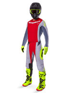 Motocrossförare i komplett racingutrustning, röd och grå tröja med Alpinestars-logotyp, 2025 Techstar Melt-byxor i klarrött och grått med neongula detaljer, klargula stövlar och handskar, svart hjälm med neongula goggles, koordinerad outfit för terrängprestanda.