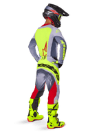 Motocross rider wearing the Alpinestars 2025 Techstar Melt Gear Set, viewed from the back. Gray jersey with a neon yellow back panel and red star logo, gray and red pants with bold neon yellow 'Alpinestars' branding across the seat, bright neon yellow motocross boots, and matching helmet.