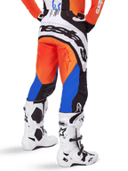 Alpinestars 2025 Techstar Melt byxor, motocrossbyxor, orange och blå, sedda bakifrån, med stor vit logotyp på sätet, bärs med matchande orange tröja och vita Tech 10-stövlar, hållbar racingutrustning för terrängkörning