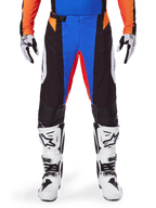 Alpinestars 2025 Techstar Melt motocrossbyxor, orange och blå, bärs med matchande tröja och vita stövlar, med svarta paneler med livfulla blå och orange accenter, perforerade för ventilation, atletisk tävlingspassform för terrängprestanda.