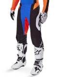 Alpinestars 2025 Techstar Melt byxor, motocrossbyxor, svarta med blå och orange detaljer, bärs med vita stövlar och matchande tröja, med hållbart skyddsmaterial och sportig racingdesign