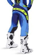 Alpinestars 2025 Techstar Melt byxor, motocrossbyxor, blå och neon-gula, vy bakifrån som visar stor gul logotyp på sätet och låren, bärs med vita motocross-stövlar och matchande blå tröja, atletisk tävlingspassform för terrängkörning