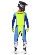 Motocrossförare klädd i Alpinestars 2025 Techstar Melt Gear Set, neongul tröja med blå och marinblå ärmar, matchande gula och blå byxor, svart och vit hjälm med goggles, vita och svarta stövlar, gula och svarta handskar, koordinerad outfit för terrängkörning