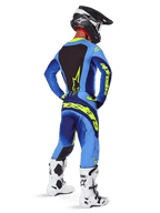 Alpinestars 2025 Techstar Melt byxor, motocrossutrustning, gul fluo och blå, vy bakifrån av förare som bär matchande blå tröja med stor gul logotyp, vita och svarta stövlar och svart hjälm, koordinerad racingoutfit för terrängprestanda