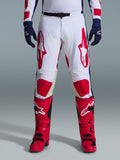 Alpinestars 2026 Racer Riway-byxor, motocrossbyxor, vita, blå och röda, bärs med röda stövlar och marinblå handskar, med stora röda logotyper på låren och röda knäpaneler, sportig förböjd design med justerbart midjespänne