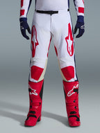 Alpinestars 2026 Racer Riway-byxor, motocrossbyxor, vita, blå och röda, bärs med röda stövlar och marinblå handskar, med stora röda logotyper på låren och röda knäpaneler, sportig förböjd design med justerbart midjespänne