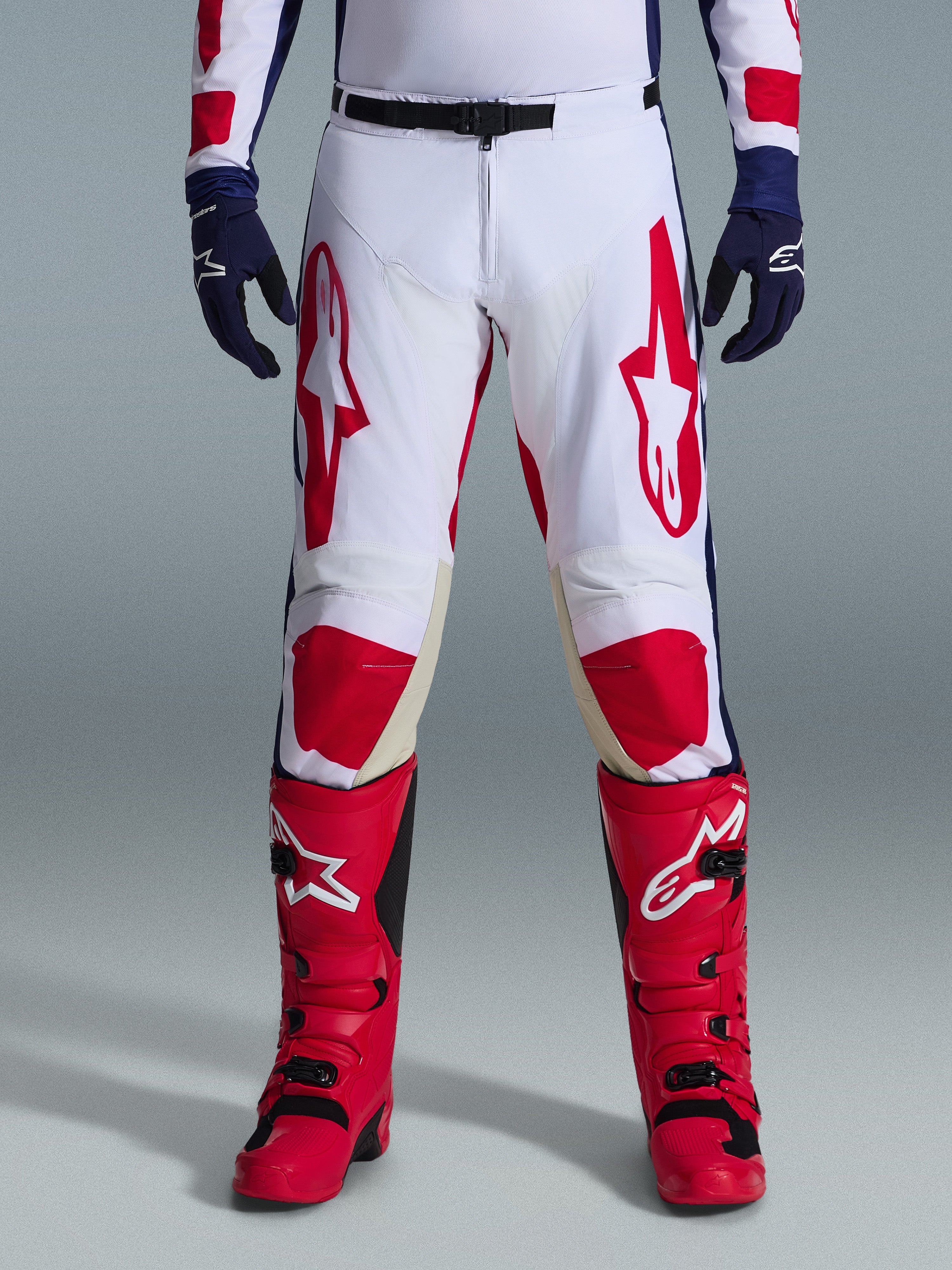 Alpinestars 2026 Racer Riway-byxor, motocrossbyxor, vita, blå och röda, bärs med röda stövlar och marinblå handskar, med stora röda logotyper på låren och röda knäpaneler, sportig förböjd design med justerbart midjespänne