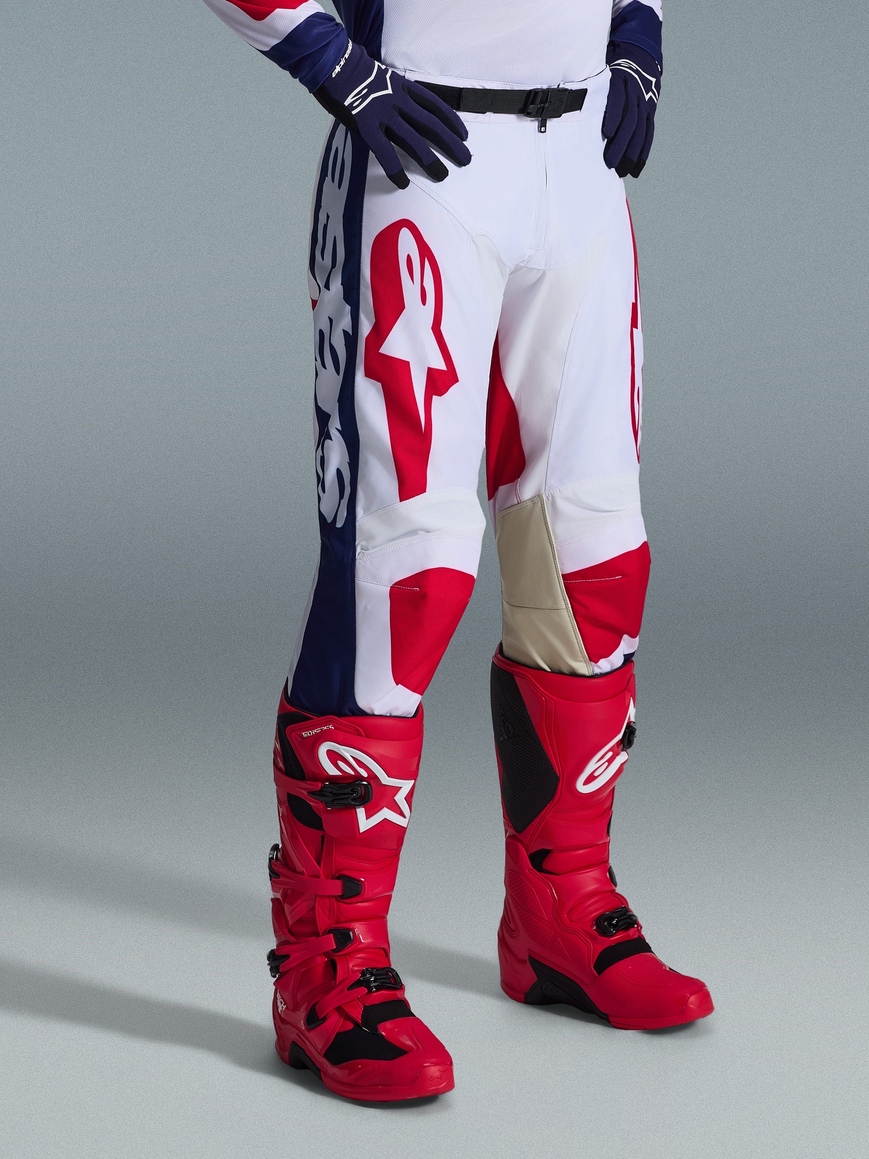 Alpinestars 2026 Racer Riway byxor, motocrossbyxor, vit blå röd, med framträdande röda logotyper på låren och blå sidopaneler med vit grafik, bärs med röda stövlar och mörkblå handskar, ergonomisk design för terrängkörning