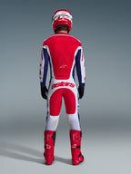 Motocrossförare sedd bakifrån i full racingutrustning, Alpinestars 2026 Racer Riway-byxor i vitt, blått och rött med matchande tröja, röda stövlar och hjälm, stor 'astars'-logotyp på sätet, koordinerad motocrossoutfit.