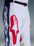 Alpinestars 2026 Racer Riway byxor, motocrossbyxor, vit, blå och röd, närbild av övre delen av benet och midjan som visar en stor röd stjärnlogotyp på vitt polytyg, blå sidopaneler med branding och svart justerbart midjebälte med SX2-magnetspänne, sportig racingdesign för terrängkörning.