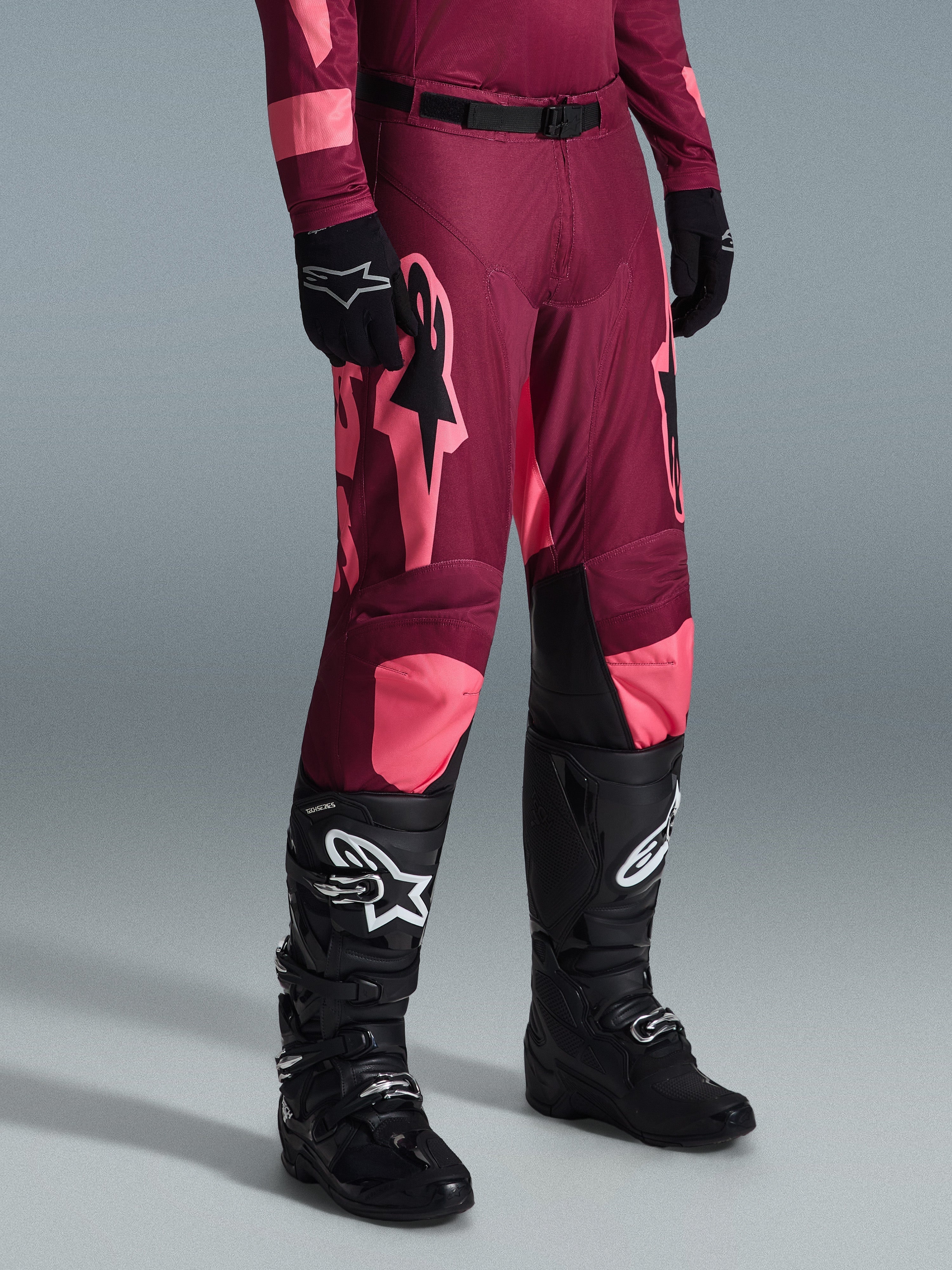 Alpinestars 2026 Racer Riway byxor, motocrossbyxor, Dark Red Coral, med stora rosa stjärnlogotyper och svarta paneler på insidan av knäna, bärs med svarta motocross-stövlar och svarta handskar, atletisk race-passform för terrängkörning