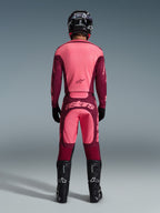 Motocrossförare sedd bakifrån klädd i Alpinestars 2026 Racer Riway-tröja och matchande byxor i Dark Red Coral, med svarta stövlar, en svart hjälm och svarta handskar, koordinerad högpresterande utrustning för terrängkörning