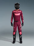 Motocross rider wearing the Alpinestars 2026 Racer Riway Gear Set, maroon jersey with pink 'astars' branding, matching maroon pants with pink knee and leg accents, black helmet, black gloves, and black boots, complete performance outfit for off-road racing