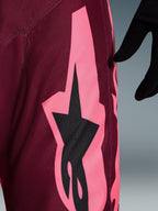 Alpinestars 2026 Racer Riway-byxor, motocrossbyxor, Dark Red Coral, närbild som visar en stor korallrosa vinkelformad grafik och svart stjärnlogotyp, som framhäver den slitstarka texturen i polytyg och prestandasömmar