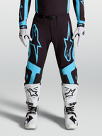 Alpinestars Supertech Vesta byxor, racingbyxor för motocross, svarta och turkosa med stora stjärngrafiker och knäpaneler i läder, bärs med matchande utrustning och vita stövlar.