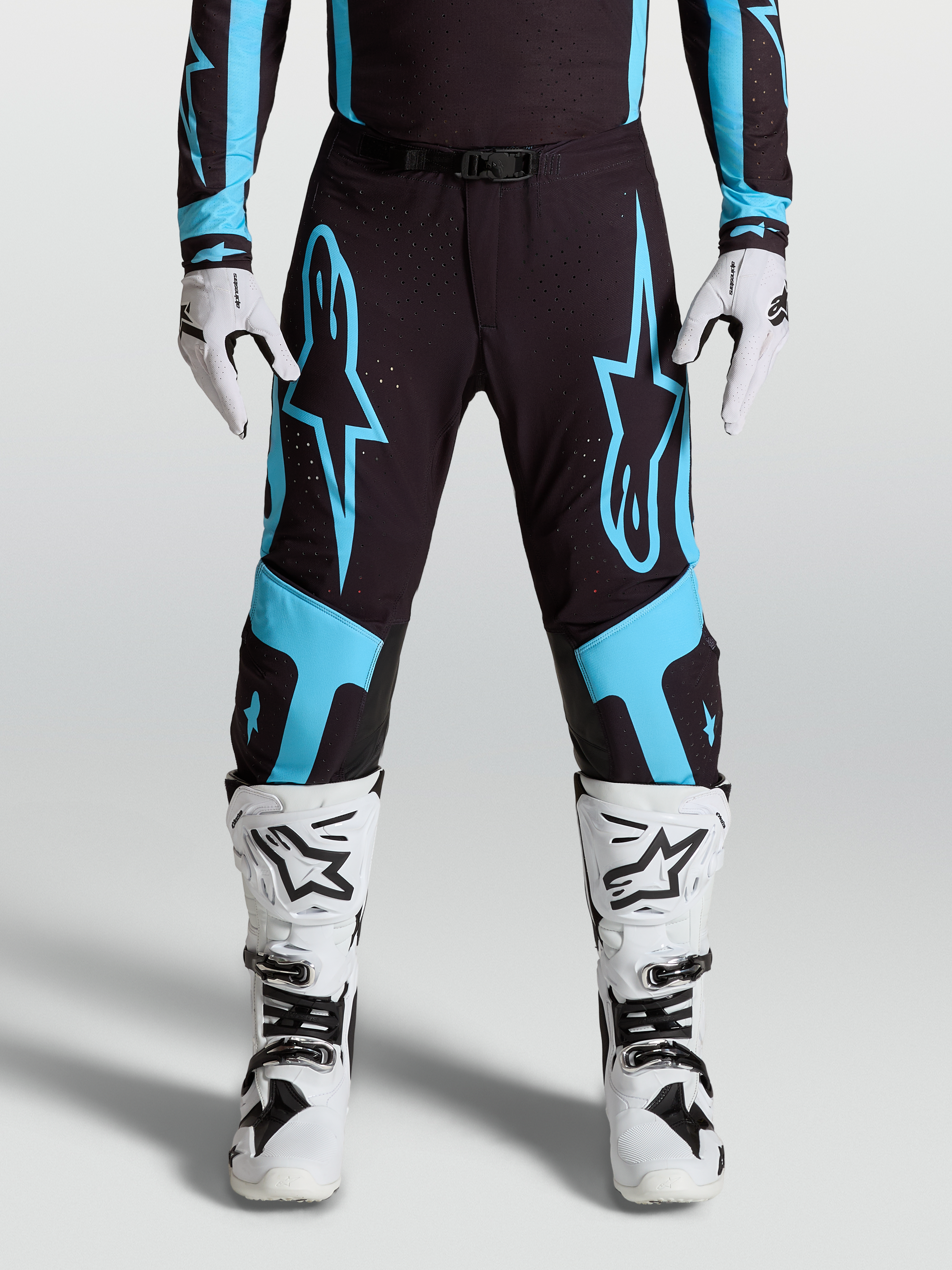 Alpinestars Supertech Vesta byxor, racingbyxor för motocross, svarta och turkosa med stora stjärngrafiker och knäpaneler i läder, bärs med matchande utrustning och vita stövlar.