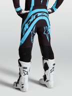 Alpinestars Supertech Vesta byxor, svarta och turkosa motocrossbyxor, vy bakifrån på modell med vita racingstövlar