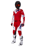 Alpinestars 2025 Racer Veil byxor, motocrossbyxor, klarröda och vita, burna som en del av en komplett racingutrustning inklusive en matchande röd och vit tröja, svart hjälm med orange goggles, vita stövlar och röda handskar, med tydliga blå Alpinestars-logotyper.