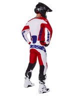 Alpinestars 2025 Racer Veil byxor, motocrossbyxor, klarröda och vita med blå detaljer, sedda bakifrån på en förare i full utrustning, framträdande Alpinestars-logotyp, ventilerande paneler på underbenen, matchande vita stövlar och svart hjälm.