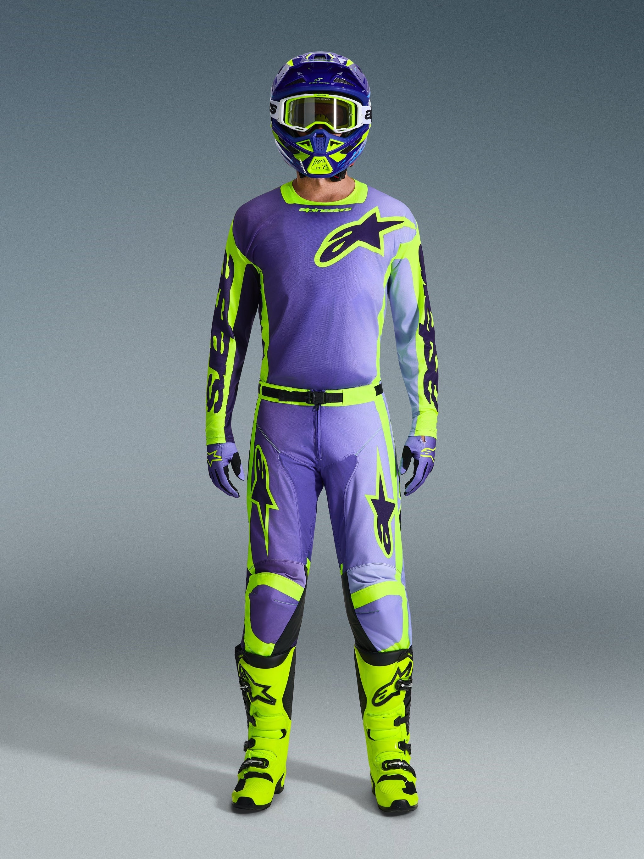 Alpinestars 2026 Racer Portl-byxor och matchande utrustningsset, motocrossförare i lila och gul fluo, med matchande tröja, hjälm, goggles och klar-gula stövlar, designade för prestanda vid terrängkörning.