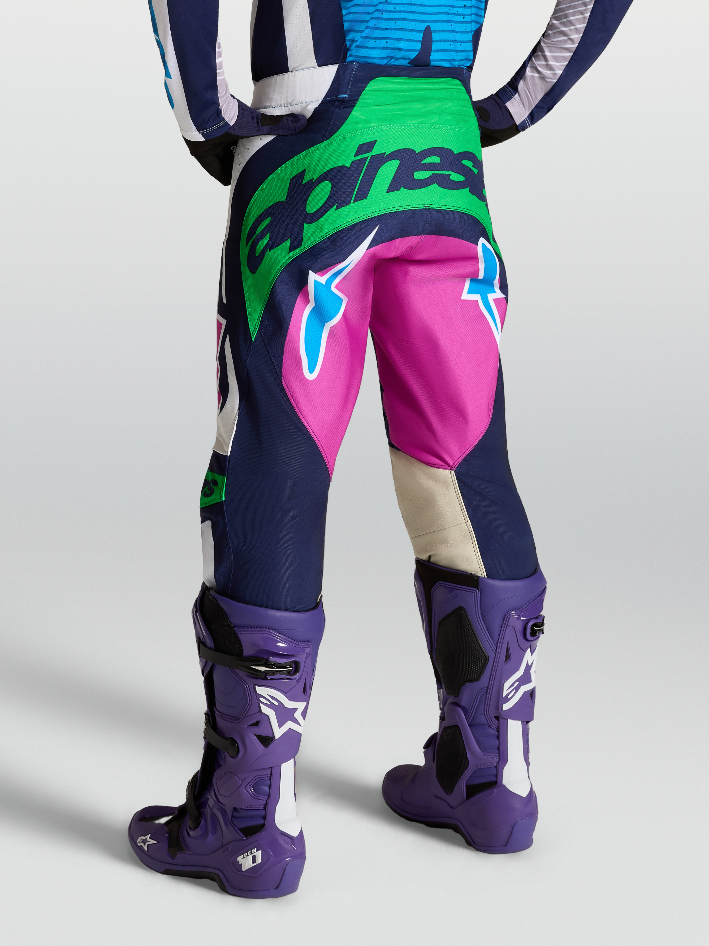 Alpinestars Techstar Maven byxor, motocrossbyxor i blått och grönt, vy bakifrån på modell med lila Tech 10 stövlar.