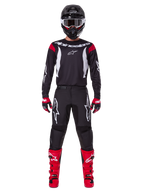 Alpinestars 2025 Fluid Haul utrustningsset, motocrossförare i komplett racingutrustning, svart tröja med röda axeldetaljer och vita logotyper, svarta byxor med vit stjärnlogotyp, klarröda stövlar, röda och svarta handskar, svart hjälm med vita goggles, koordinerad outfit för terrängkörning