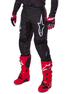 Alpinestars 2025 Fluid Haul byxor, motocrossbyxor, svarta med en stor vit Alpinestars-logotyp, bärs med klarröda stövlar och rödsvarta handskar, slitstark 600D polytygskonstruktion med ergonomisk skärning för terrängkörning