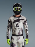 Motocrossförare klädd i Alpinestars 2026 Racer Lahnd-tröja, Sand Camo-mönster i grått och vitt, stor svart Astar-logotyp och branding på bröstet, matchat med svart hjälm, neongula goggles och handskar, prestandautrustning för terrängkörning