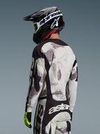 Motocrossförare bakifrån i 2026 Racer Lahnd Jersey i Sand Camo, grå och vit abstrakt mönstrad tröja med svarta detaljer, matchad med svart Alpinestars-hjälm, vita goggles och neongula handskar, visar ryggprofil och passform för terrängkörning.